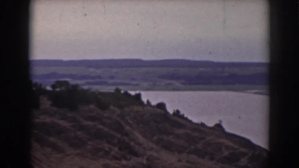 Final 1938 New Hampshire frame showing a hillside foreground, lake water, distant hills, muted sky, and dark 8mm frame edges.