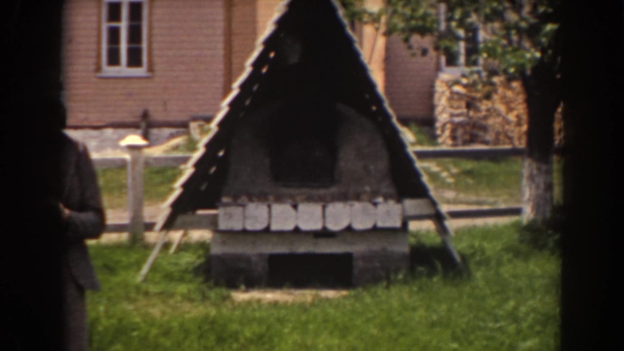 Triangular rustic stone structure in a grassy yard with a partial person at the left edge.