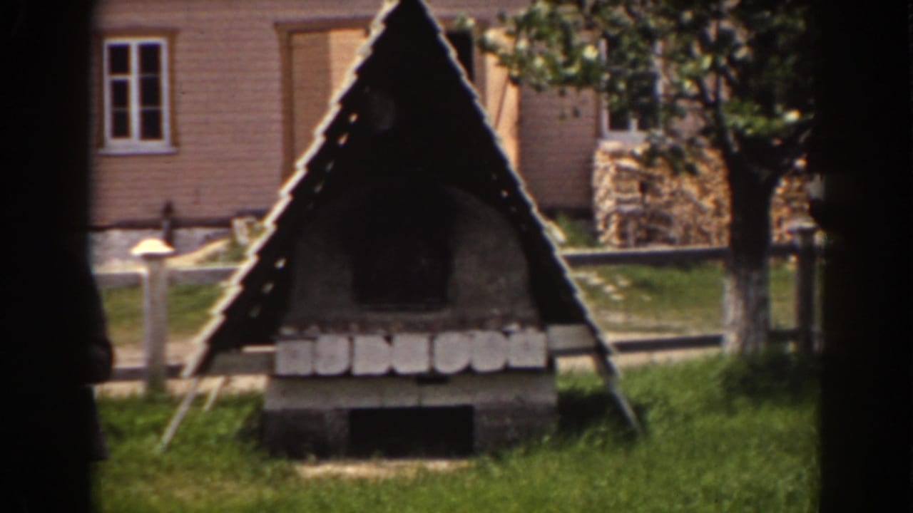 1938 Mount Washington view of the rustic triangular structure, with grass, fence, house windows, trees, and a cropped person near frame left.