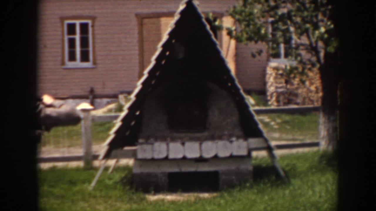 1938 Mount Washington frame showing the rustic triangular structure in a grassy yard, with fence rails, trees, and a house facade behind it.