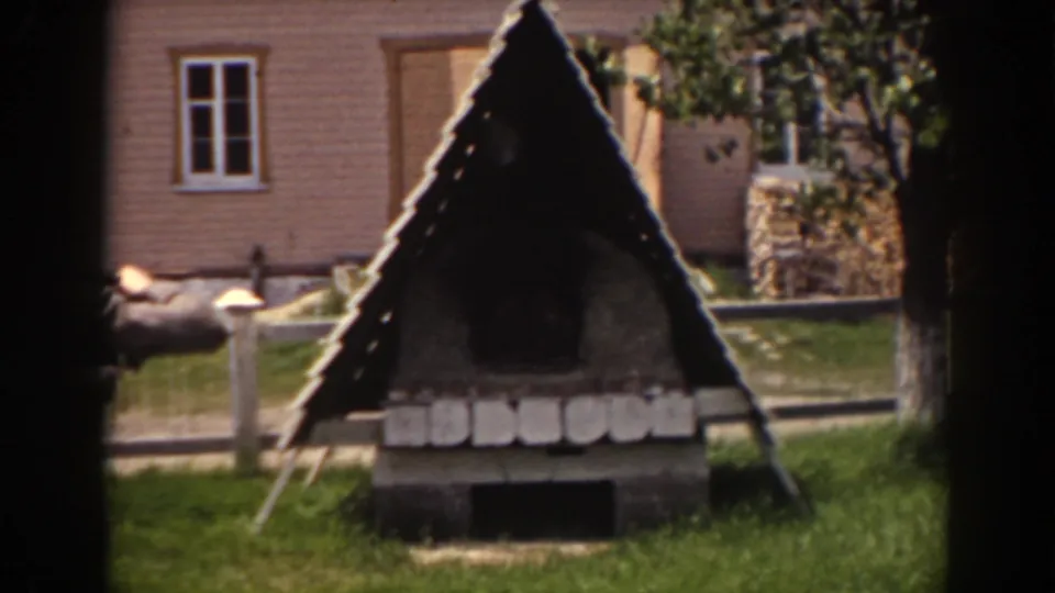 1938 Mount Washington frame showing the rustic triangular structure in a grassy yard, with fence rails, trees, and a house facade behind it.