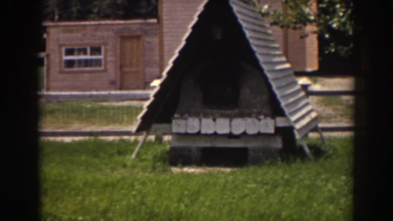 1938 Mount Washington footage shows a dark A-frame yard structure, brick outbuilding, grass, and trees in bright daylight.