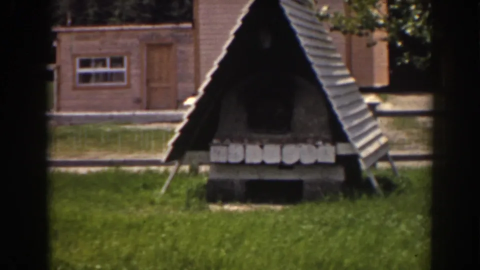 1938 Mount Washington footage shows a dark A-frame yard structure, brick outbuilding, grass, and trees in bright daylight.