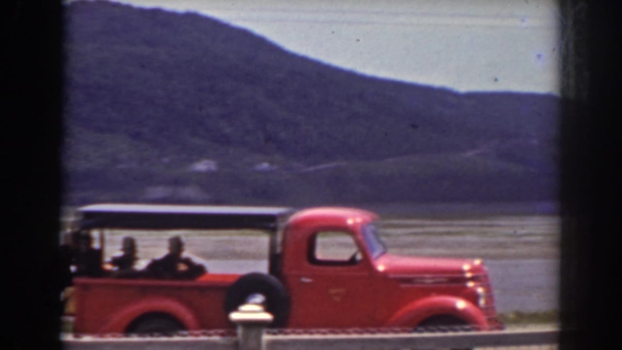 Red pickup truck and riders continue along a Mount Washington lakeside road in 1938 home-movie footage.