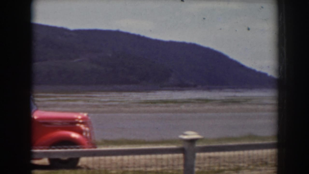 The front of the red pickup crosses the lower frame, leaving a clear view of lake water and wooded hills behind it.