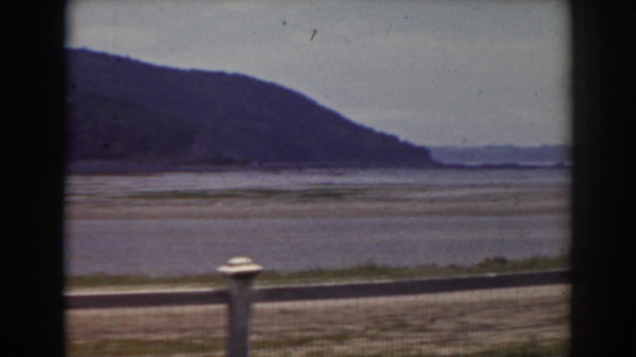 A quiet roadside view near Mount Washington, New Hampshire, showing fence posts, a broad riverbed, and distant hills.