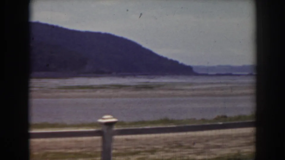A quiet roadside view near Mount Washington, New Hampshire, showing fence posts, a broad riverbed, and distant hills.
