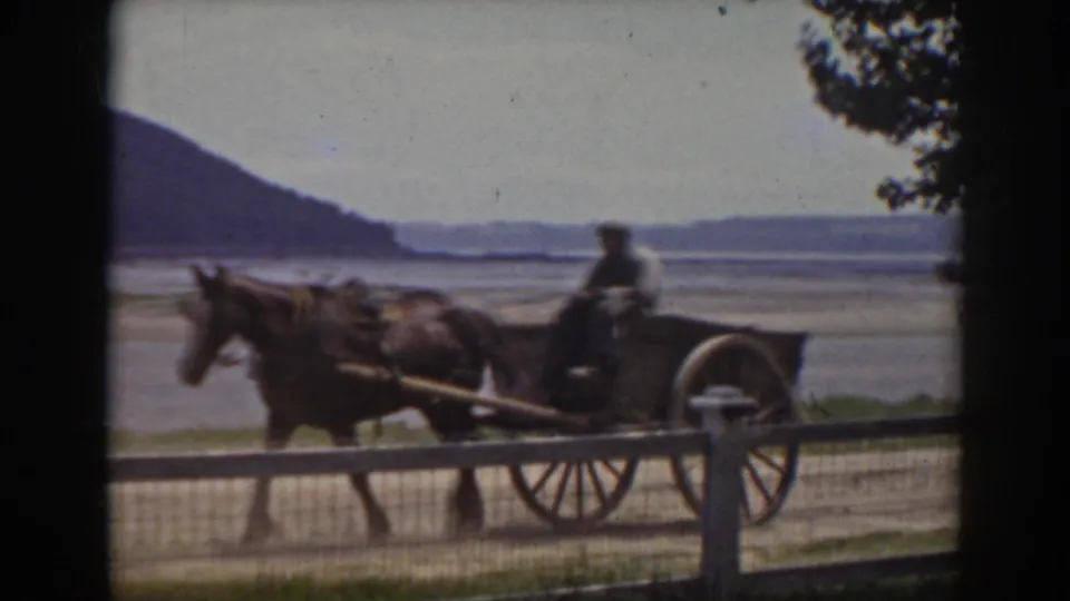 The horse-drawn cart moves across the roadside frame, with the driver silhouetted against the New Hampshire riverbed and hills.