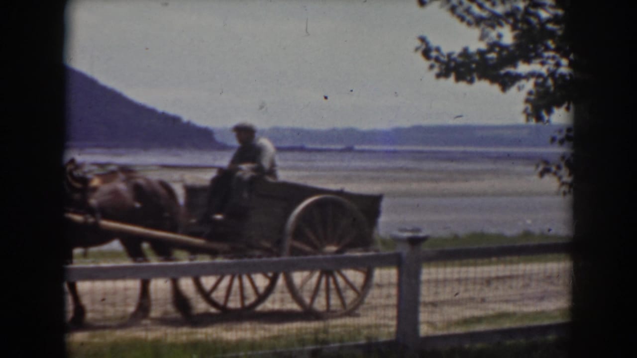 Horse-drawn cart passes a fence with water and hills beyond.