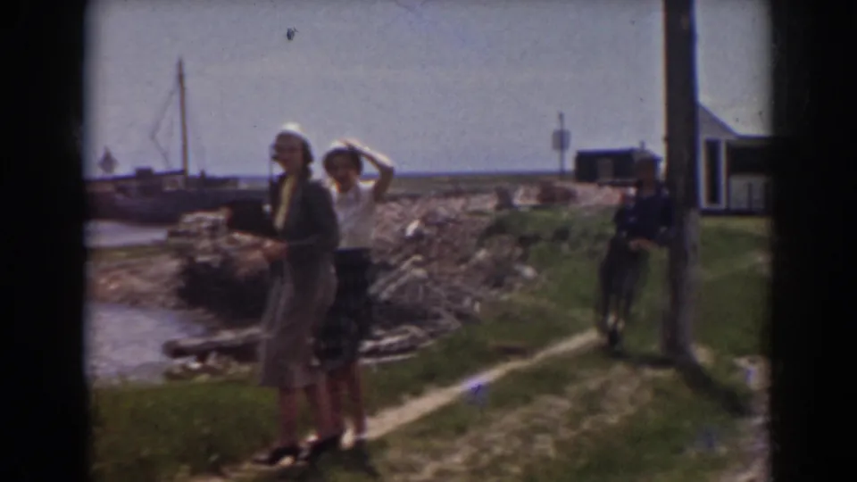 Two women in 1930s-style clothing stand near a rocky shore and boats in the Mount Washington, New Hampshire clip.