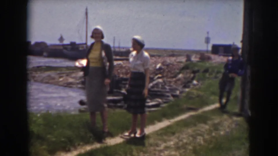 Two women wearing skirts and hats stand by the water in 1938 home-movie footage from New Hampshire.