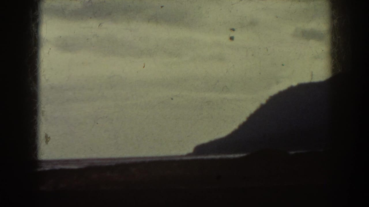 Dark window frame over a pale sky, calm water, and a silhouetted ridge.