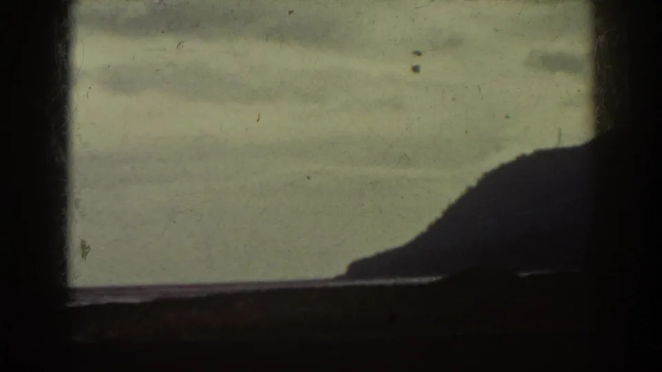 1938 Mount Washington area home-movie frame showing a dark window grid, pale cloudy sky, calm water, and a distant silhouetted ridge.
