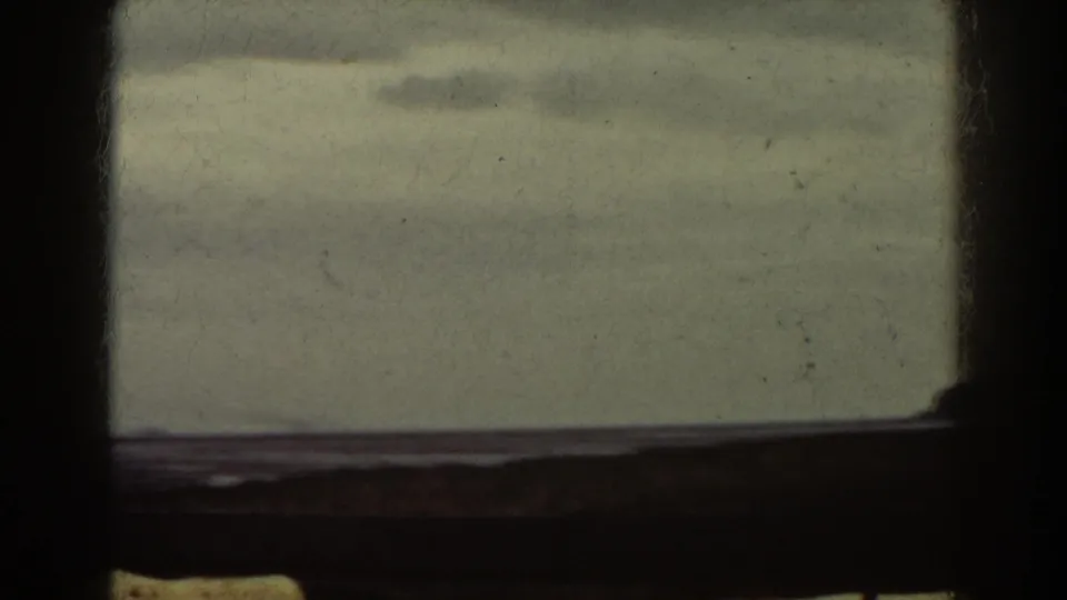 1938 Mount Washington area home-movie frame where lower window panes divide a muted shoreline view of pale water, sky, and faint horizon.