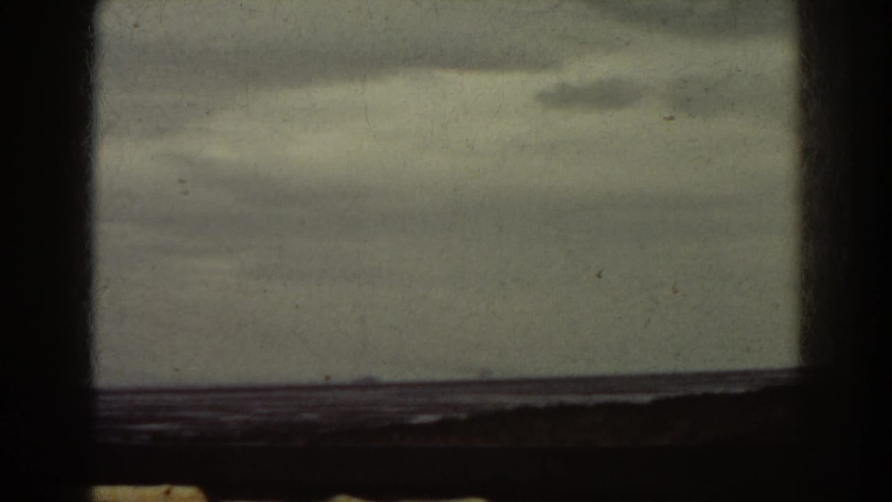 Cloudy sky over dark water with a distant low landform and heavy film borders.