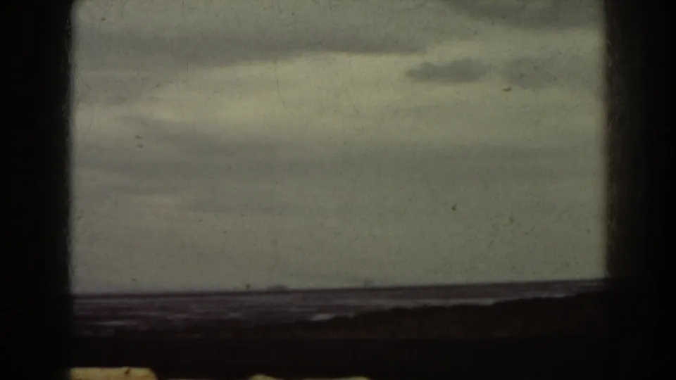 1938 8mm frame showing overcast sky, water, and a distant dark landform, with visible film gate borders.