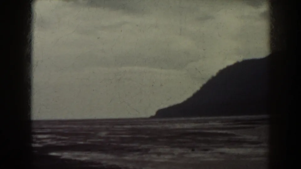 1938 8mm frame with a dark landform silhouette on the right, rippled water below, and cloudy sky above.