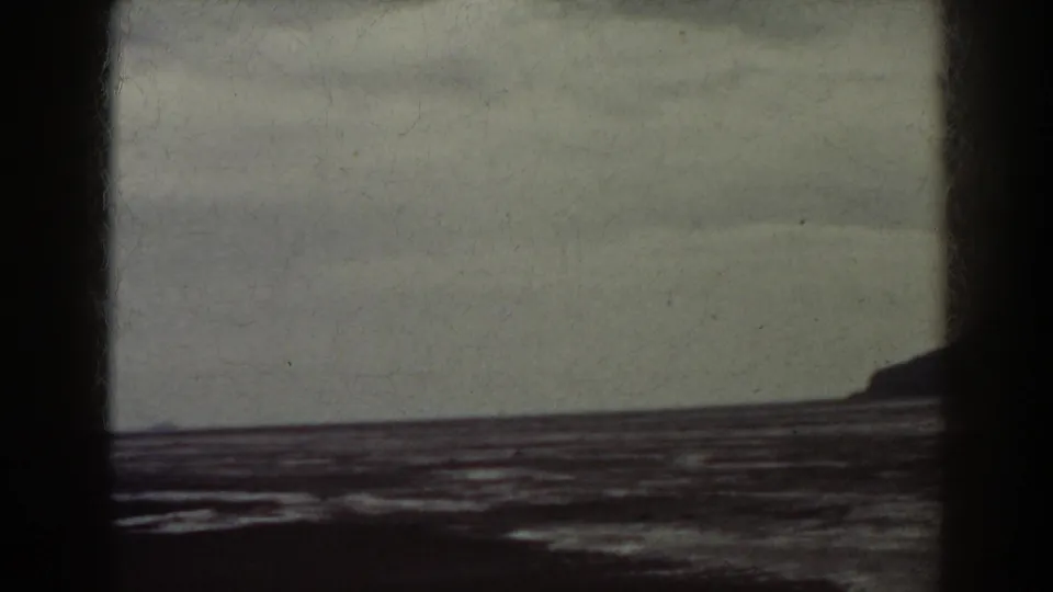 1938 8mm frame showing water, overcast sky, and a small dark landform at the right edge of the composition.