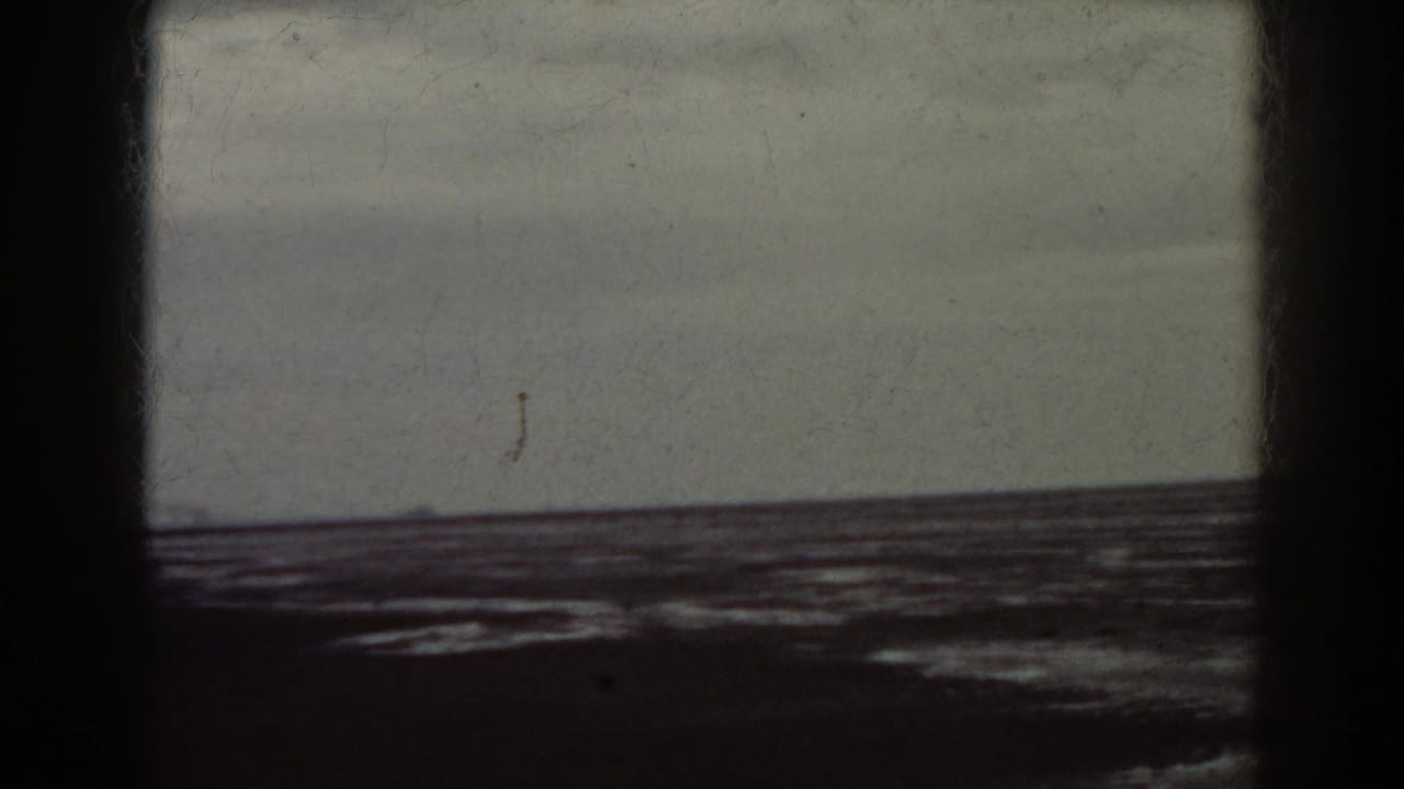 Overcast sea view with a low horizon, dark shoreline, and heavy black film borders.