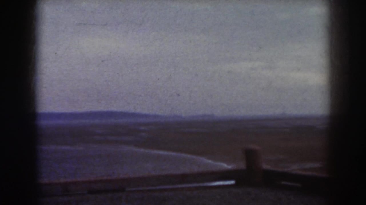 Open plain and distant ridge viewed through a dark vertical frame with a post near the foreground.
