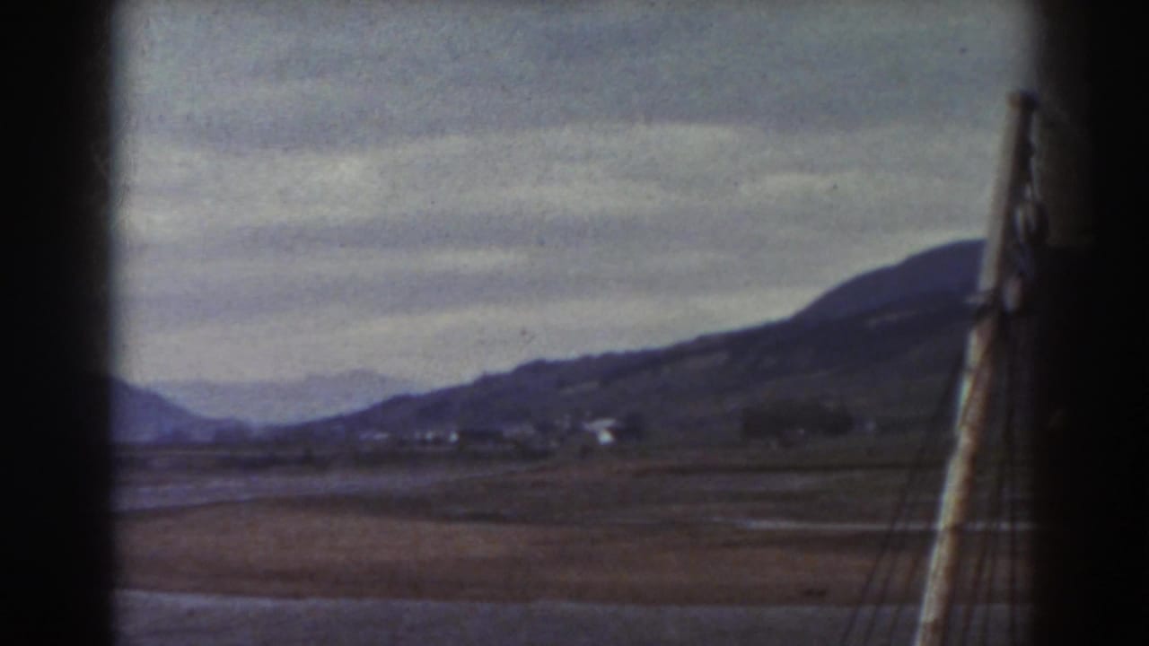 Overcast water and brown fields seen through dark vertical frame edges.