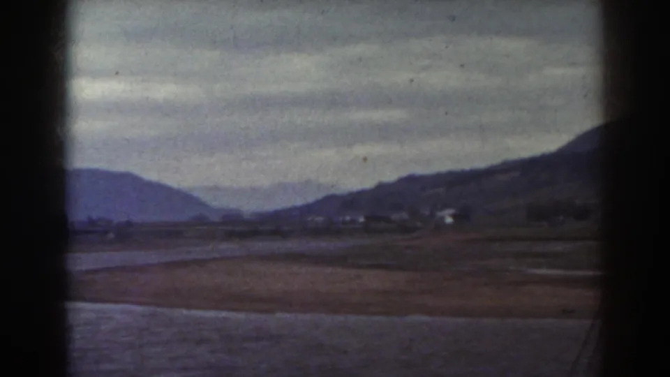 Rural New Hampshire landscape with water, brown field, rolling hills, and a clouded sky in soft 8mm color.