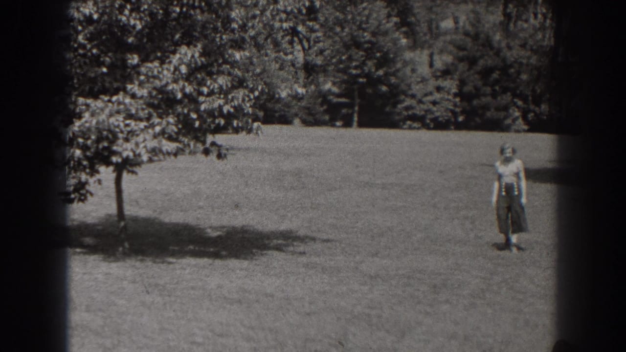 A woman in a light blouse and dark skirt stands on a grassy New Jersey park lawn in 1938 footage.
