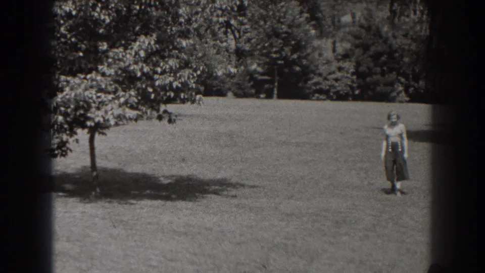 A woman in a light blouse and dark skirt stands on a grassy New Jersey park lawn in 1938 footage.
