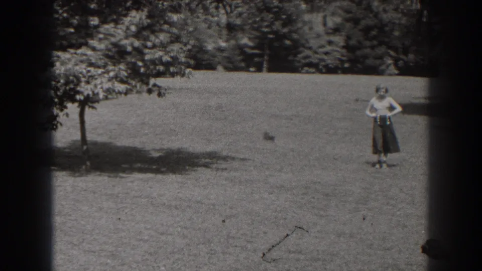 The woman faces the fixed 8mm camera while standing on a grassy park lawn in New Jersey.
