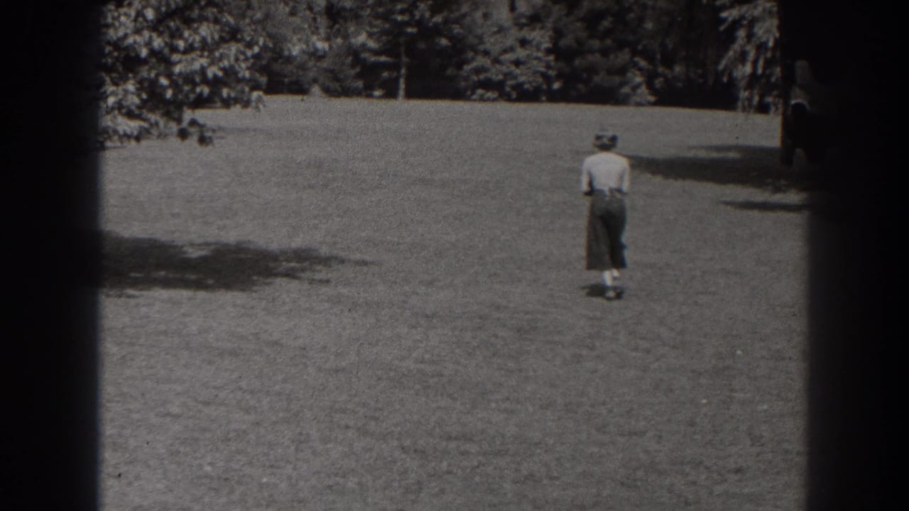 Woman seen from behind walking across a grassy field toward trees.
