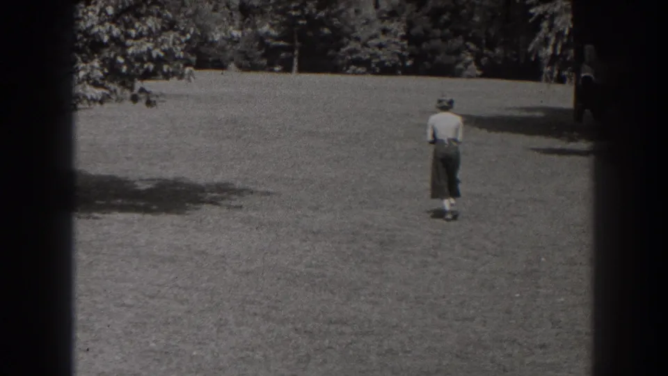 In black-and-white 1938 New Jersey 8mm footage, a woman walks away across an open grassy field toward a distant tree line.