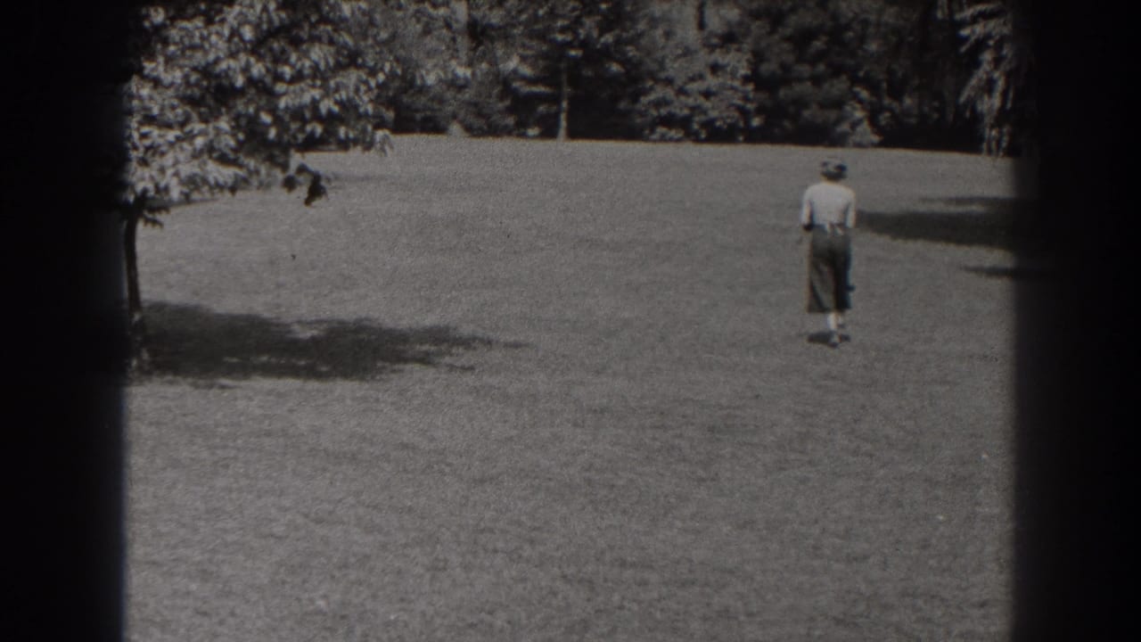 The woman appears smaller as she continues across the grassy New Jersey field, framed by trees and 8mm gate shadows.