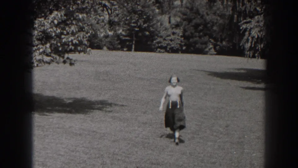 In 1938 New Jersey home-movie footage, a woman walks across an open grassy park toward the camera, with trees behind her.