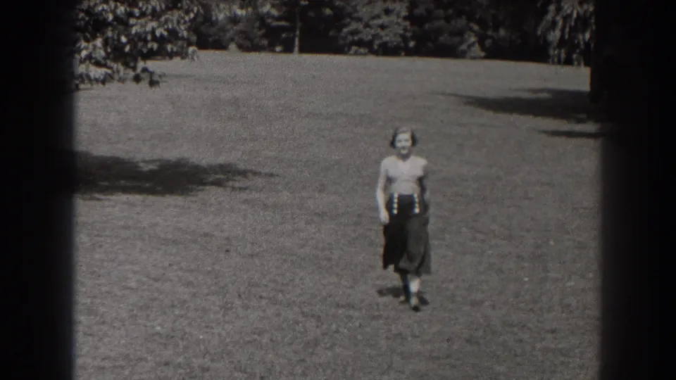 A woman in a blouse and dark skirt faces the camera on an open lawn in the 1938 New Jersey park scene.
