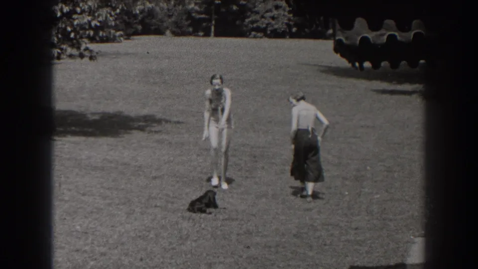 A 1938 New Jersey home-movie frame shows two young women separated on a lawn, with a small black dog sitting or standing near the center.