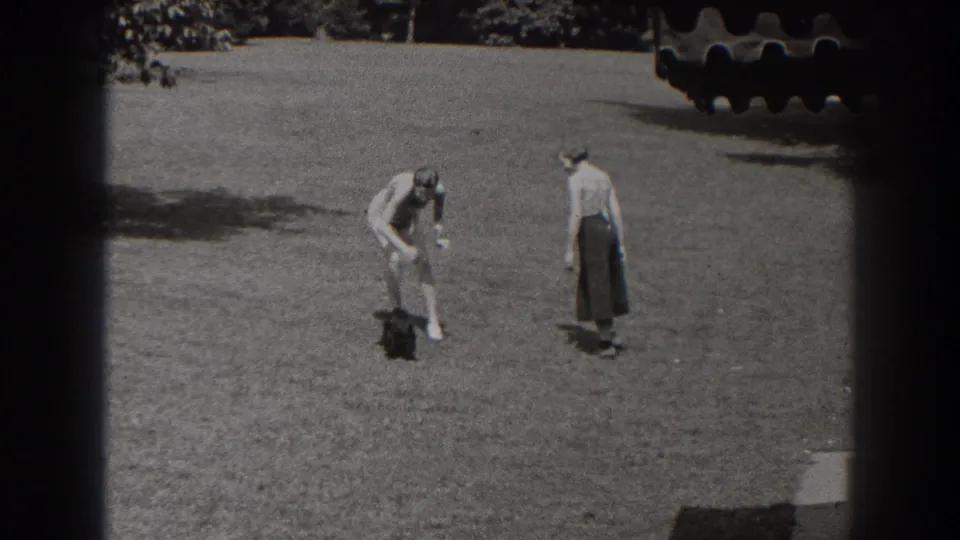 The 1938 New Jersey home movie shows both women focused on the small black dog, with one bending low and the other standing nearby on the grass.