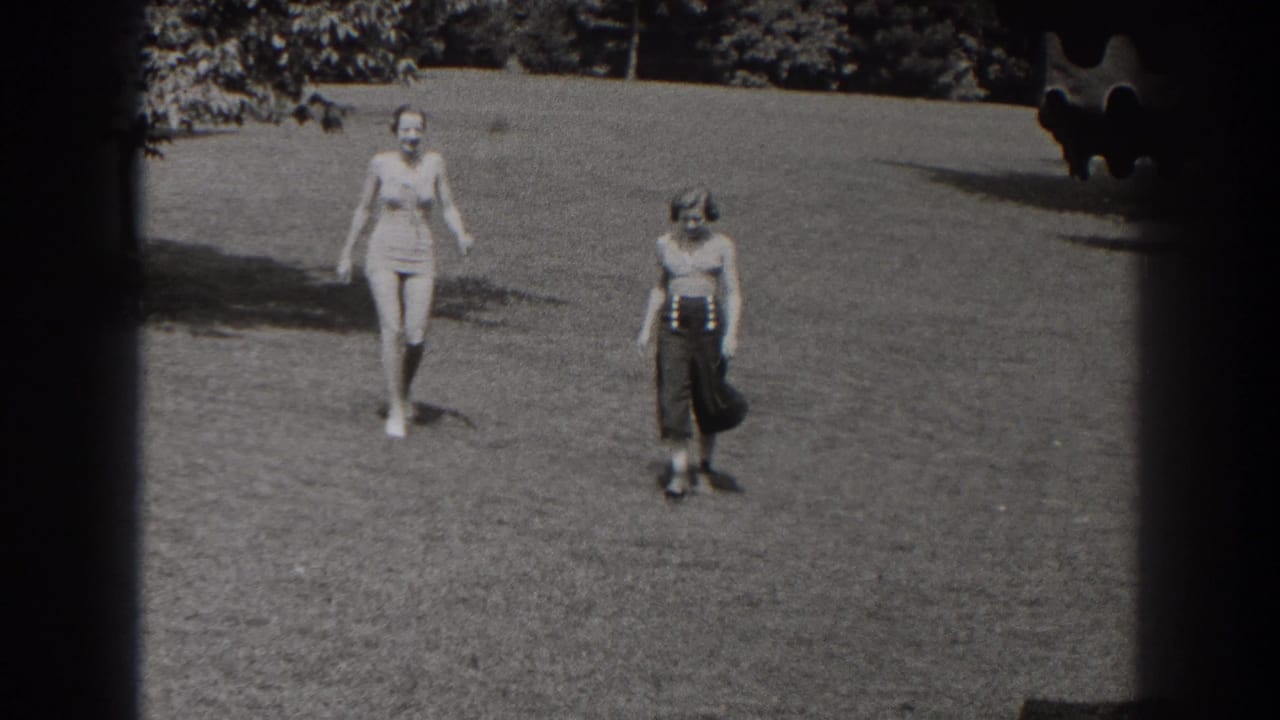 Two women in a 1938 New Jersey park scene walk toward the camera across open grass, with trees and film borders visible.
