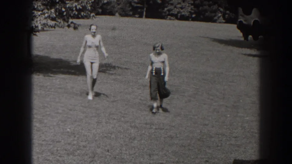 Two women in a 1938 New Jersey park scene walk toward the camera across open grass, with trees and film borders visible.