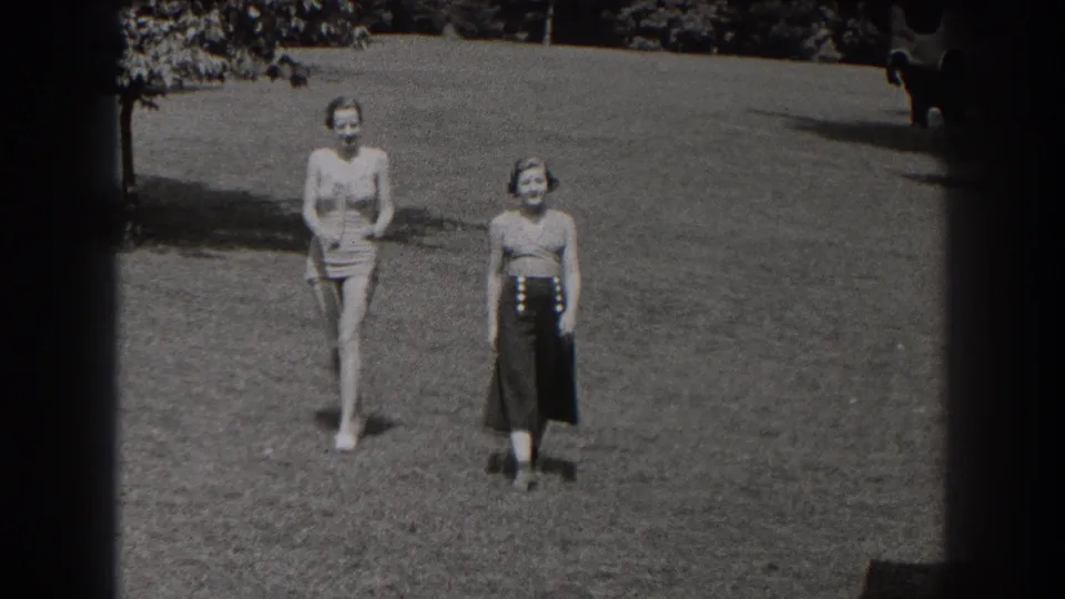 The women are closer to the camera in the New Jersey park footage, walking side by side over the grass in bright daylight.
