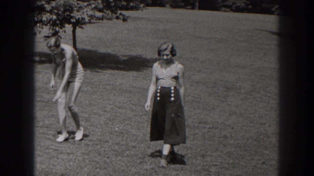 Two women on a grassy lawn, one bending forward and one facing the camera in a dark skirt.