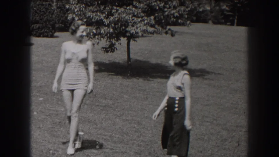 In a 1938 New Jersey field scene, two women walk apart across the grass as one turns in profile and the other faces the camera.