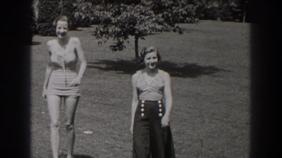 Two women in 1938 New Jersey outdoor home-movie footage smile as they approach the camera across a grassy field.