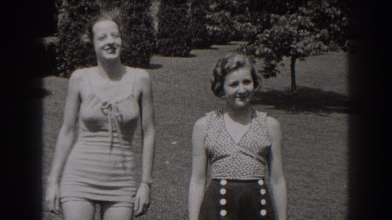 Two women smile while standing or walking on a lawn in swimwear.
