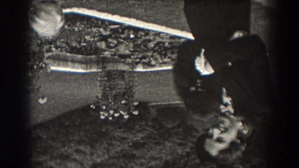 1938 New Jersey 8mm frame showing reflected outdoor figures, with a dark-suited woman near a light-suited person on a wet or glossy surface.