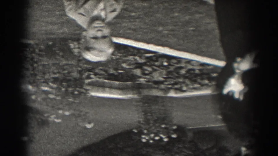 Black-and-white 8mm frame from New Jersey showing an upside-down reflection of a light-suited figure beside a partial dark-clothed person.