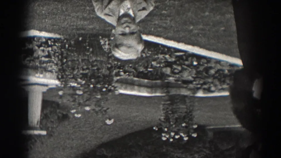 1938 New Jersey home-movie frame, upside down, with shrubs, lawn, a pale garden structure, and a partial figure near the frame edge.