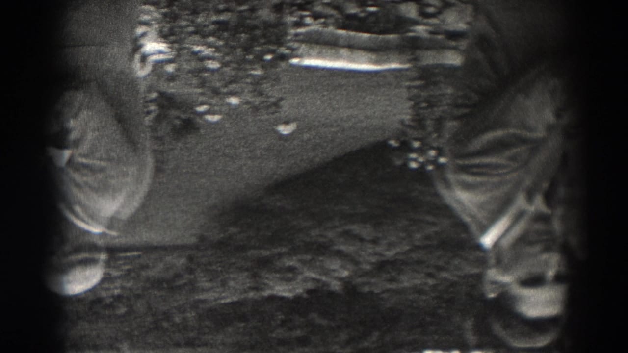 1938 New Jersey home-movie frame showing adult men in suits and brimmed hats near tables, with the view inverted and heavily vignetted.