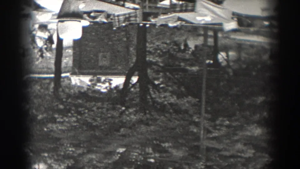 1938 New Jersey home-movie view with a prominent street lamp, a larger building facade, trees, poles, and nearby rooftops.
