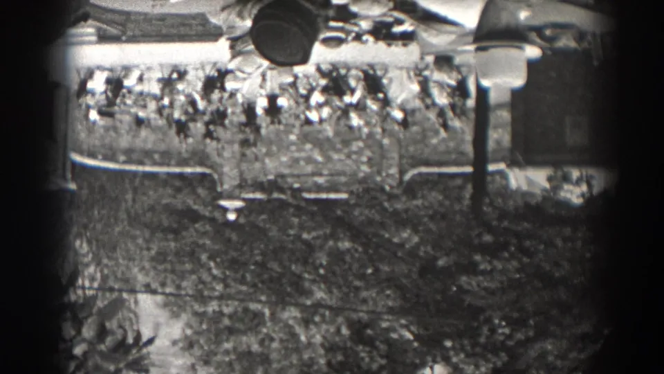1938 New Jersey home-movie frame showing a distant seated crowd at an outdoor venue, partly obscured by trees and film-frame edges.
