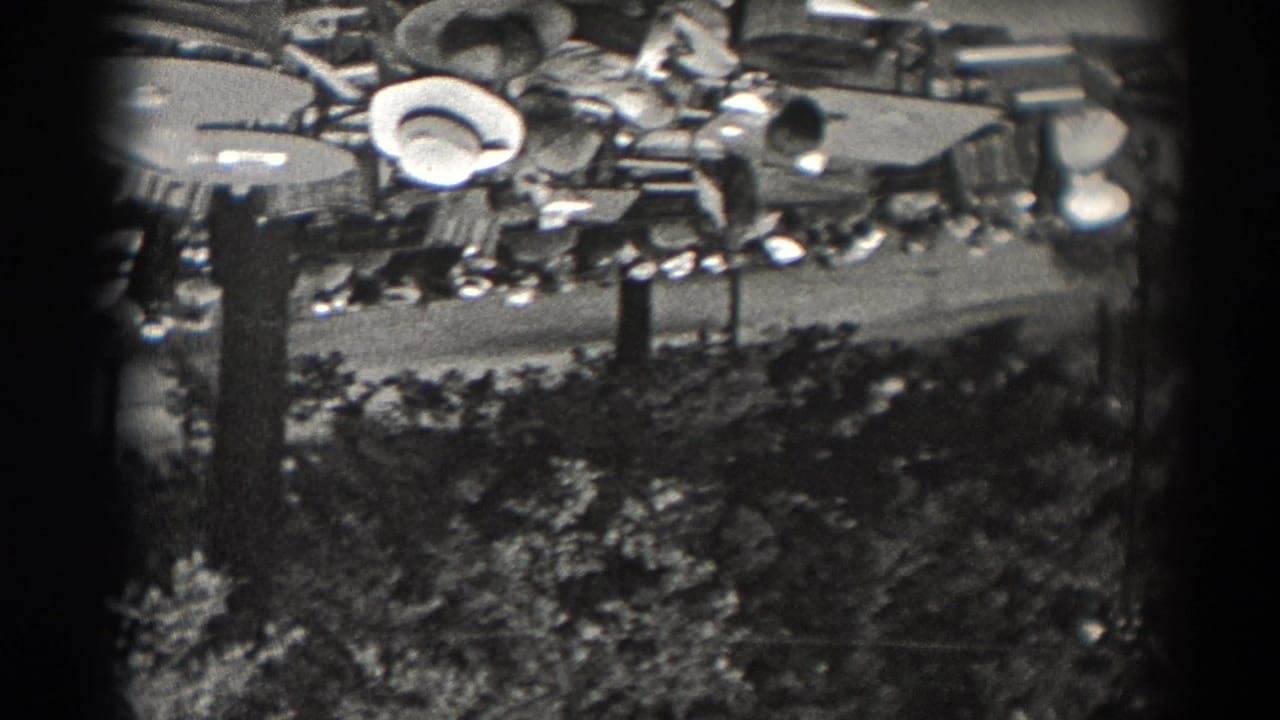 Elevated 1938 New Jersey frame with spectators or visitors near an outdoor venue, framed by trees, lamp posts, and visible film borders.